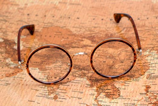 Photo of glasses on a map of a world, antique style. Focus on China. May be used as illustration for traveling theme.