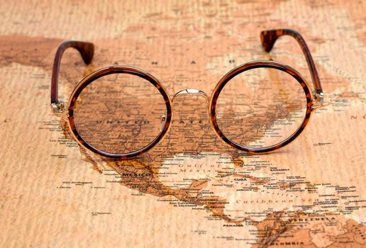 Photo of glasses on a map of a world, antique style. Focus on United States. May be used as illustration for traveling theme.