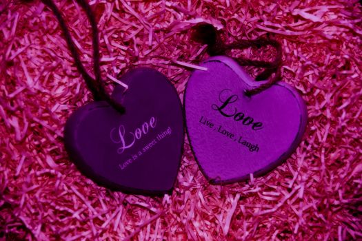 two pink wooden love hearts in a love nest made of straw with loving inscriptions