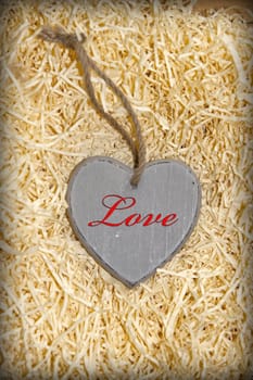 single grey wooden love heart in a love nest made of straw inscribed in red