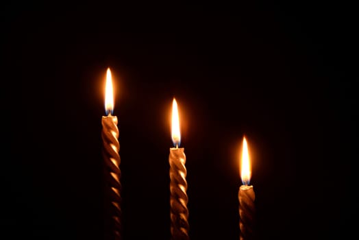 Photo of three golden candles burning on a black background.
