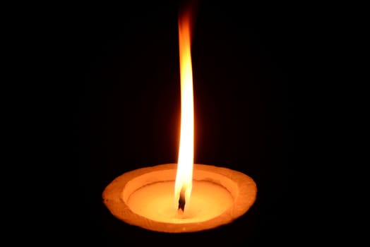 Photo of a white candle with stone candlestick burning on a black background.