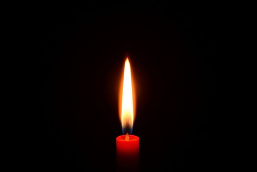 Photo of a red candle burning on a black background.