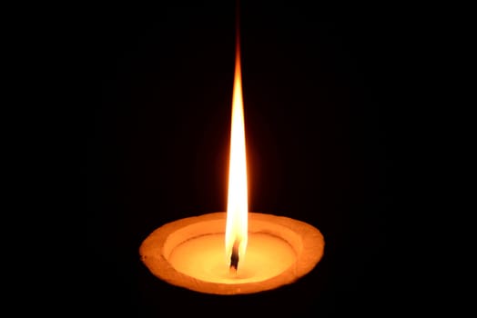 Photo of a white candle with stone candlestick burning on a black background.