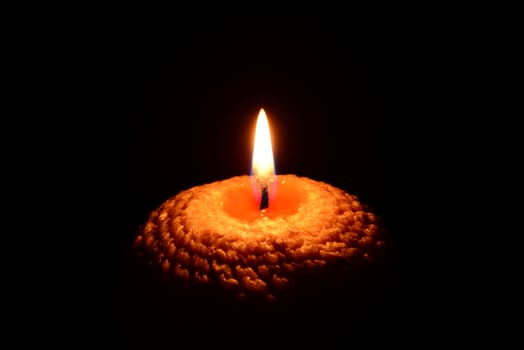 Photo of a yellow candle with a wavy pattern burning on a black background.