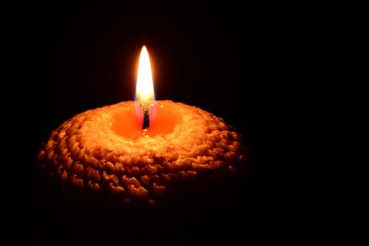 Photo of a yellow candle with a wavy pattern burning on a black background.