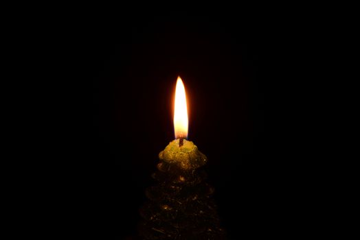 Photo of a green christmas tree shaped candle burning on a black background.