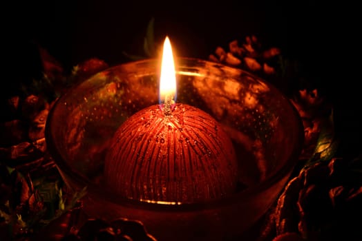 Photo of a red christmas candle on a plate burning on a black background.