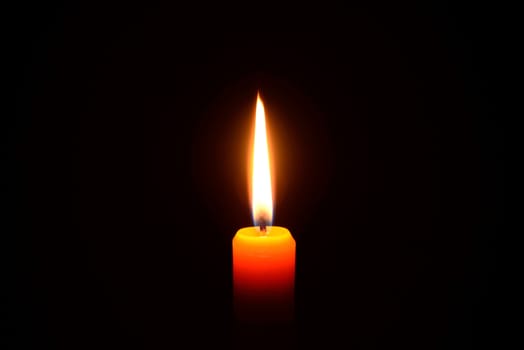 Photo of an orange candle burning on a black background.