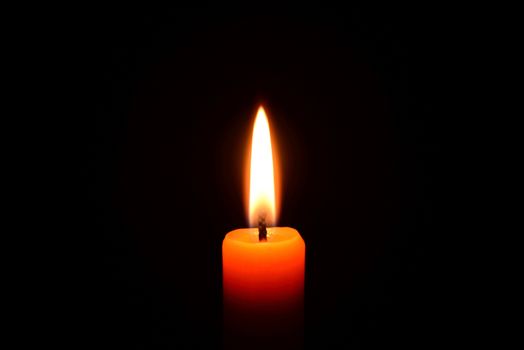 Photo of an orange candle burning on a black background.