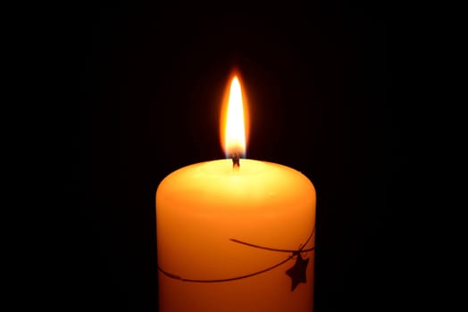 Photo of a white christmas candle burning on a black background.