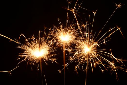 Photo of three burning christmas sparklers on a black background