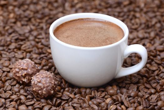 Photo of a cup of coffee with candies. White color cup on a brown coffee beans background. Food photography.