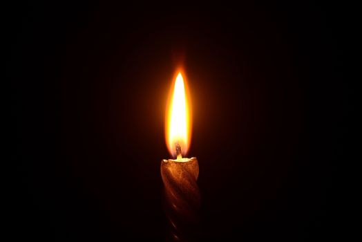 Photo of a golden candle burning on a black background.