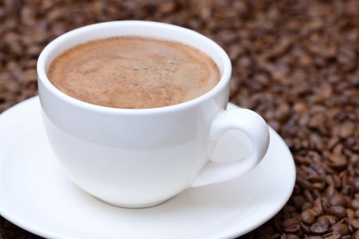 Photo of a cup of coffee with on a saucer. White color cup on a brown coffee beans background. Food photography.