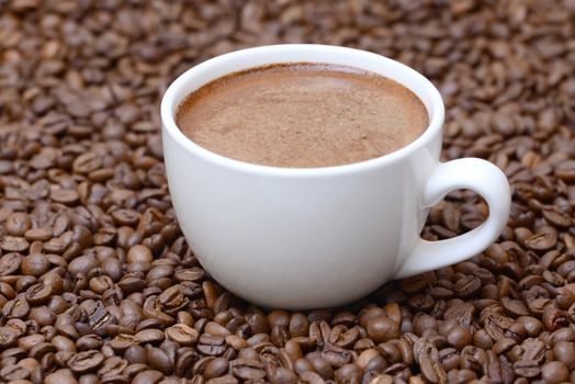 Photo of a white color cup on a brown coffee beans background. Food photography.