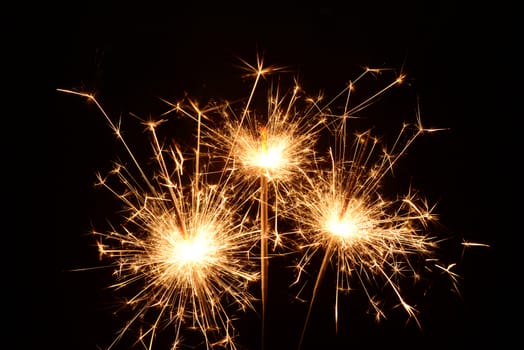 Photo of three burning christmas sparklers on a black background
