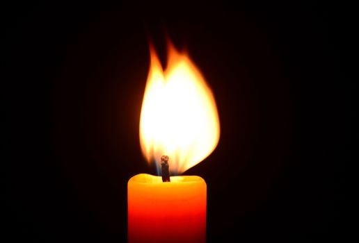 Photo of an orange candle burning on a black background. Objects photography.