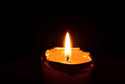 Photo of a golden candle burning on a black background. Objects photography.