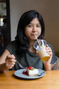 Asian woman drinking tea with strawberry cheesecake at cafeteria