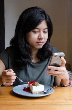 Young asian woman chating mobile phone with a cake in cafe