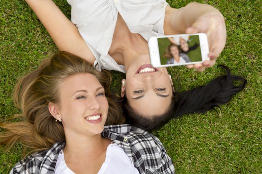 Female best friends lying on the grass and taking selfies