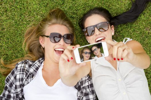 Female best friends lying on the grass and taking selfies