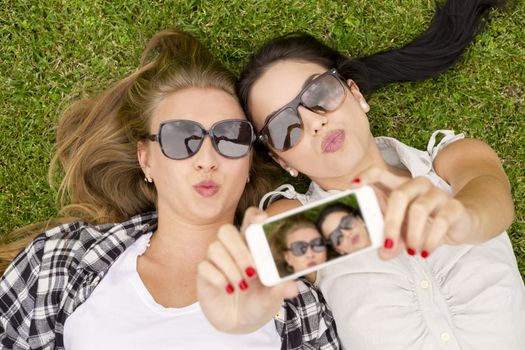 Female best friends lying on the grass and taking selfies