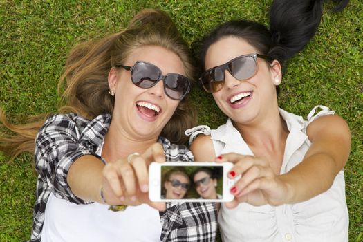 Female best friends lying on the grass and taking selfies