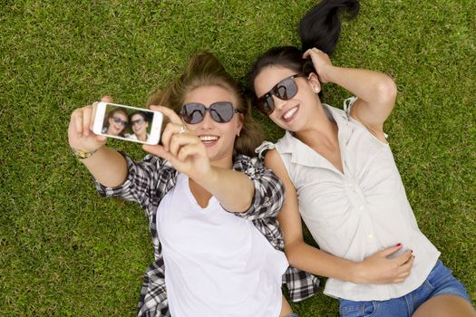 Female best friends lying on the grass and taking selfies