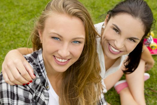 Teens best friends sitting on the grass smiling and having a good time