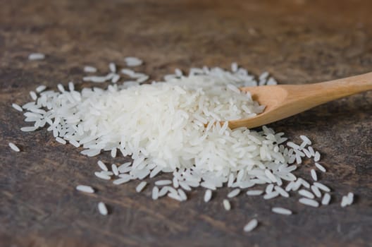 white rice  grains with wooden spoon on wooden table