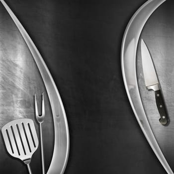 Modern blackboard with metal frame, kitchen utensils and knife on brushed steel background. Template for recipes or a food menu