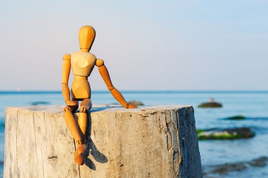 Wooden female figure sitting on the stump at the sea