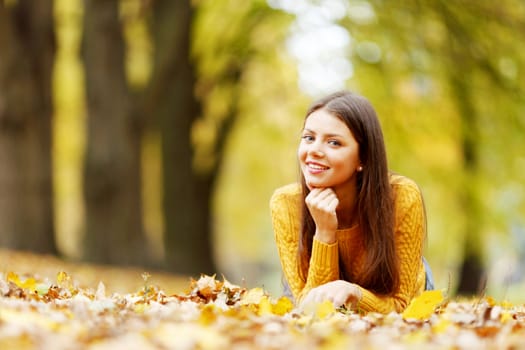 Young cute woman laying on dry leaves in autumn park