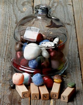 Delicious Colored Gum and Hard Candies in Glass Jar with Lid and Wooden Letters closeup on Rustic Wooden background