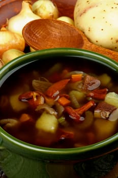 Delicious Vegetarian Soup with Chanterelle Mushrooms  in Green Pot with Raw Ingredients and Wooden Spoon closeup