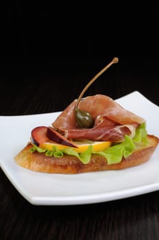 A slice of jamon on toast with lettuce, lemon, plum and capers