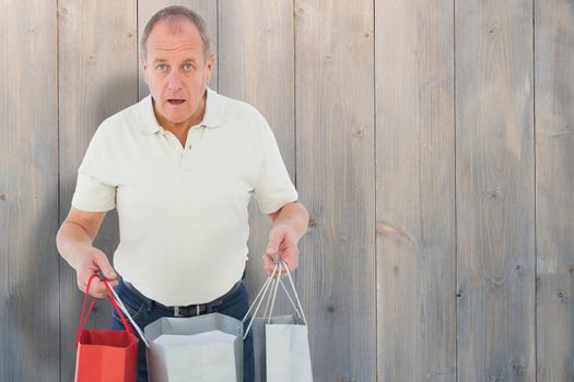 Shocked man holding shopping bags against pale grey wooden planks