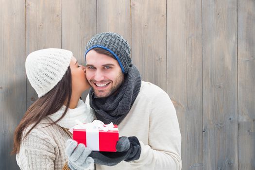 Winter couple holding gift against pale grey wooden planks