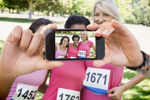 Composite image of hand holding smartphone showing photograph of breast cancer activists