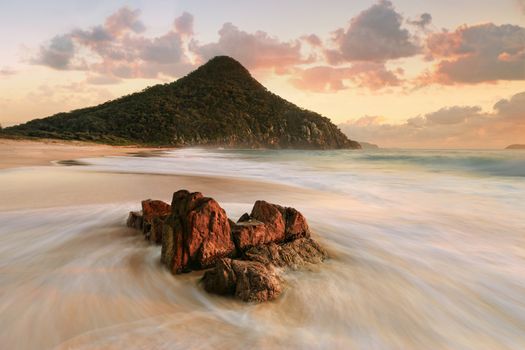 Zenith Beach views of Mt Tomaree in the first rays of morning light and ocean flows around foreground rocks. Zenith Beach is on the mid north coast of NSW a popular holiday spot in Port 'Stephens.