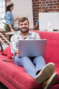 Young casual man using laptop on couch in the office