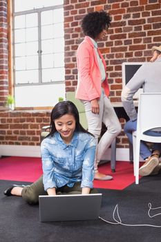 Young casual woman using laptop with colleagues behind in the office