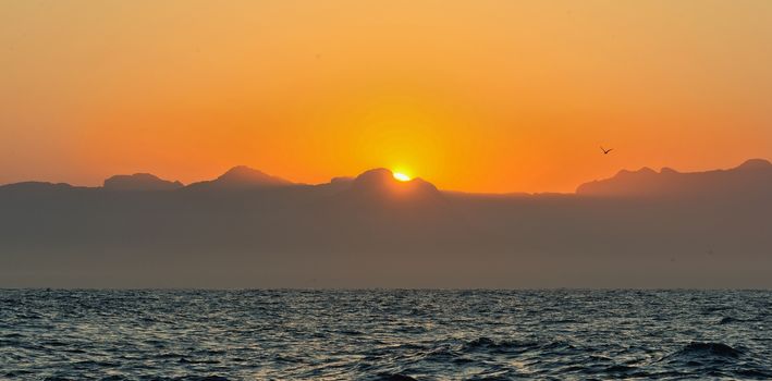 Orange sunrise at the ocean with mountains silhouettes 