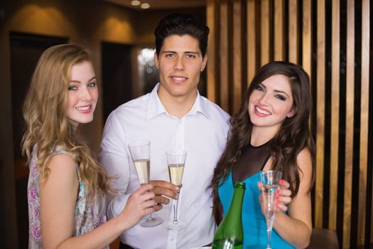 Attractive friends smiling at camera holding champagne at the bar