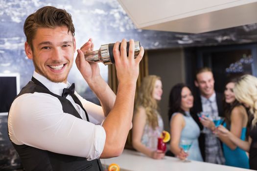 Handsome barman smiling at camera making a cocktail at the bar