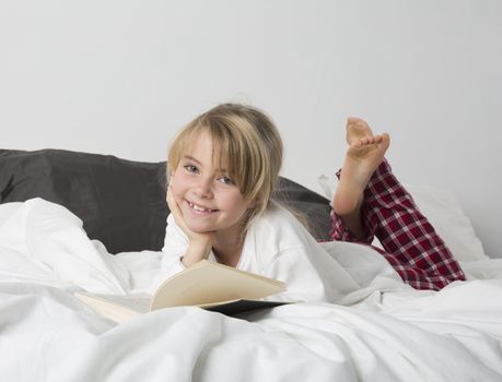 Smiling Young Girl Reading a Book in bed
