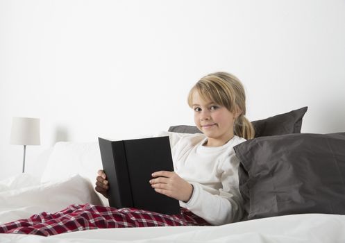 Young girl with a book in bed look in the camera