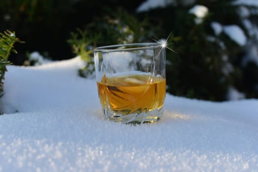 glass with ice cold whiskey in snow